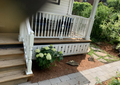 Refreshed garden bed beside a white-railed porch, with brown mulch, leafy shrubs, and white hydrangea flowers.