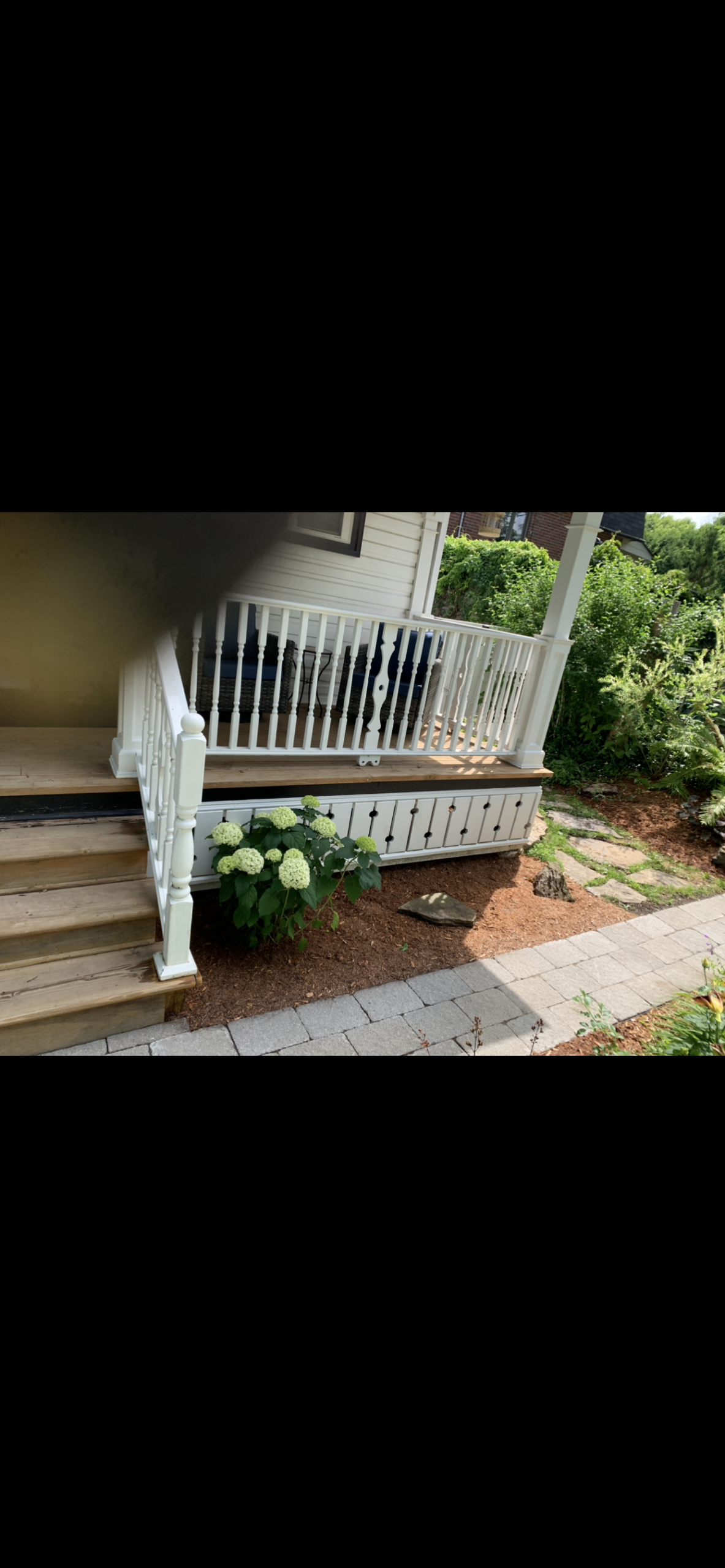 IMG_4512 Refreshed garden bed beside a white-railed porch, with brown mulch, leafy shrubs, and white hydrangea flowers.